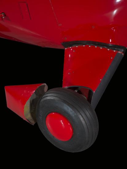 Close up of a tire and landing gear of a red painted plane.