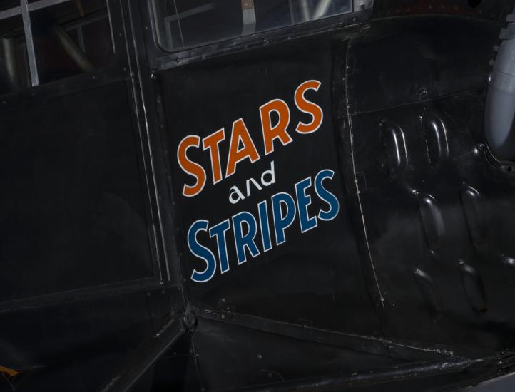 The words Stars and Stripes are painted orange and blue on the side of an airplane. 		