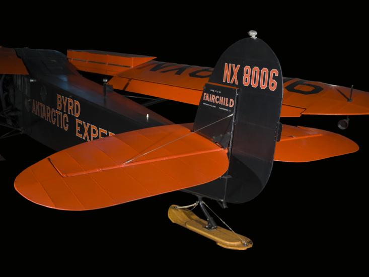 Close up of landing gear and vertical stabilizer of a blue and orange plane. 