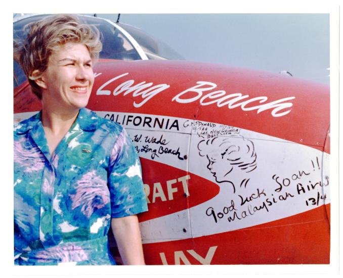 Woman posing next to the nose of a small airplane.