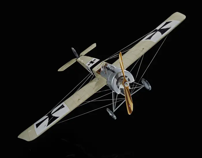Plastic exhibit model of an Imperial German Air Service Fokker E.III Eindekker monoplane in overall tan color scheme with black and white stripes on fuselage.