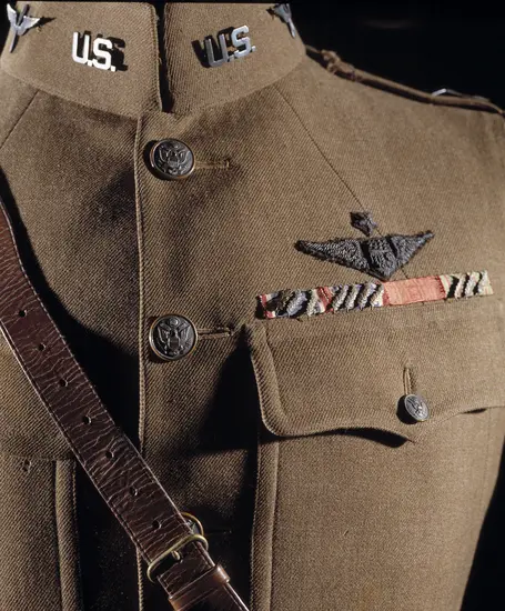 A single breasted drab wool coat with five brass buttons down front; two upper patch pockets and two lower patch pockets with brass buttoned flap; a stiff or "choker" collar; a single gold officer's lace on each cuff; a brass "U.S." insignia on right collar; a Winged Propeller Air Service insignia on left collar; three overseas service chevrons on left cuff; a Distinguished Service Cross ribbon with 7 oak leaf clusters, a French Legion of Honor ribbon, and a French Croix de Guerre ribbon with 3 palm leaves.