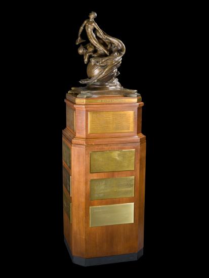 A bronze sculpture of a globe, two male and one female figures rising from the globe, sitting atop a tall walnut base.