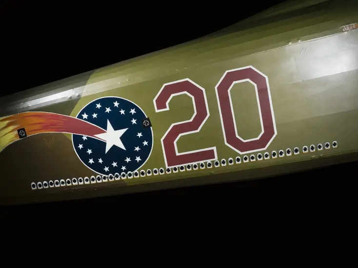 The fuselage of an airplane painted green, with an image of a shooting star and the number 20. Along the bottom are white tombstone shapes with black crosses in them. There are an impressive amount of them. 