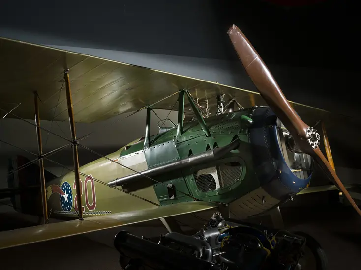 A biplane painted blue, green, and beige. The front is a large wooden propeller is on the front. The body of the airplane is painted with a comet and the number 20. 