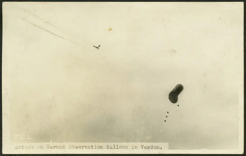 A sepia toned photograph with two objects in frame in the sky in the distance. The object on the left is much smaller and shaped like an airplane. It is pointed in the direction of the object on the right with streaks of exhaust flowing from behind it. The object on the right is a cylindrical balloon with one side beginning to deflate. It appears to be falling to the ground.