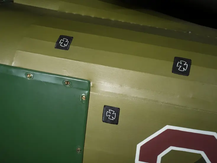 A close up shot of an airplane, with green paint. There are small black squares with crosses on it. 