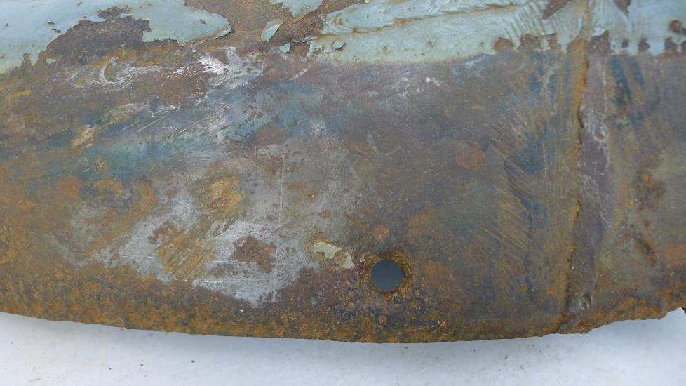 A cover section of a World War II aircraft shows a black surface underneath paint, dirt, grime, and preservatives.