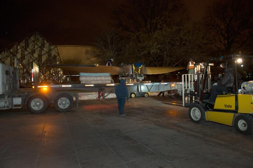 Outside of the Museum, a wind tunnel fan is transported by a truck with a large flatbed into the Museum.