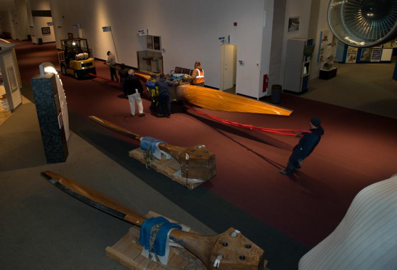 Museum staff members move parts of a large wind tunnel fan around other objects inside the Museum.