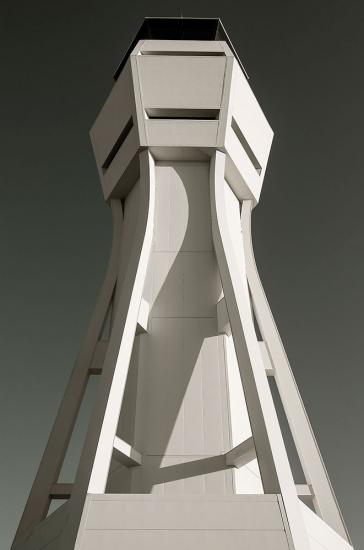 An air traffic control tower with light-colored, contemporary style supports. Near the top, a base for operations has at least three sides for different perspectives of observation.