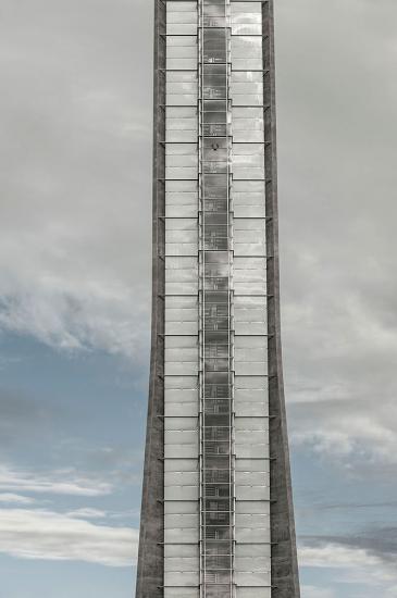 Partial view of the air traffic control at Oslo Airport in Norway. This portion of the tower has dark gray-colored steel sides which open up to possess lighter gray brick-like patterns in between another section of darker gray steel.