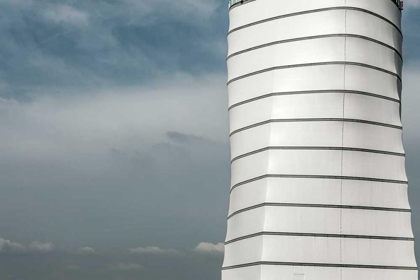 Partial view of the base of the air traffic control tower at Vienna International Airport. The base features a white, concrete structure with four sides that jut out into eight sides in the higher section.