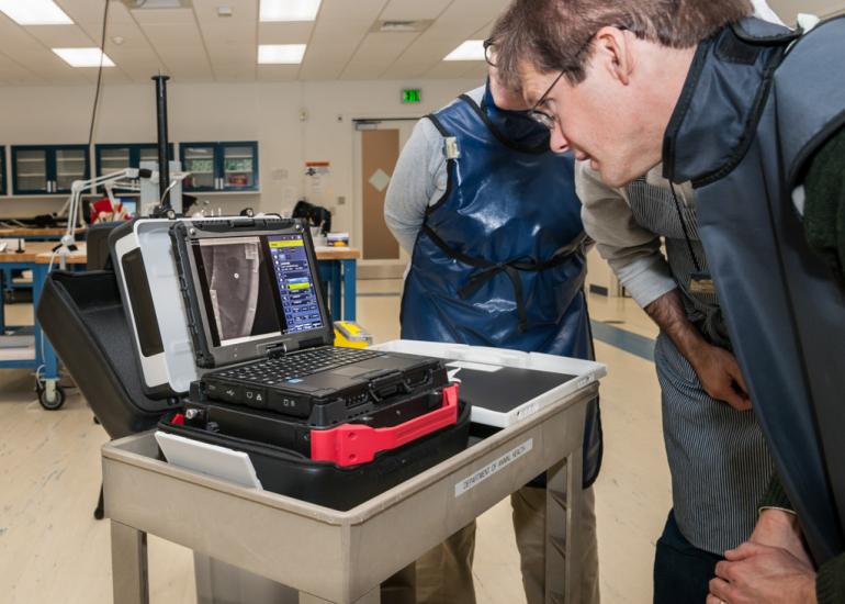 A Musuem conservator looks at a small laptop computer, where they view X-ray images of a spaceship studio model.