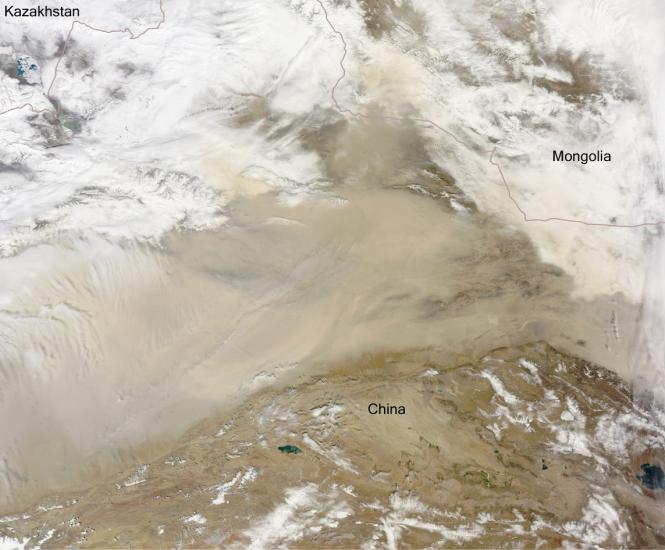 Satellite view of a desert near the border of China and Mongolia. The view is partially obscured by clouds on the top and bottom of the view as well as a dust storm in the center.