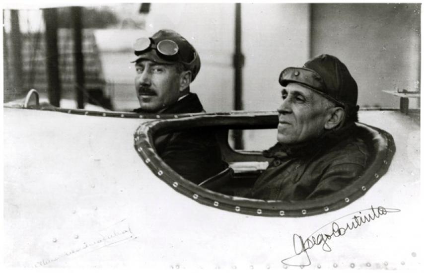 Artur de Sacadura Cabral (on the left) and Gago Coutinho (on the right), both of whom are Portuguese male naval aviators, inside the cockpit of an aircraft.