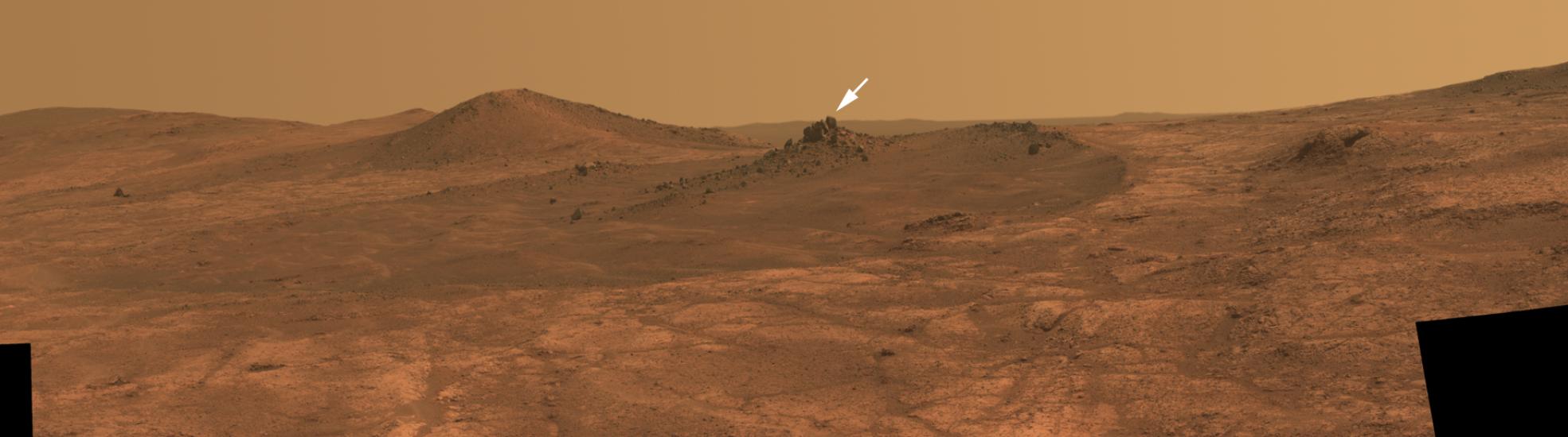 A hilly landscape on Mars with a small white arrow pointing to a crater named after a historic aircraft, the "Spirit of St. Louis".