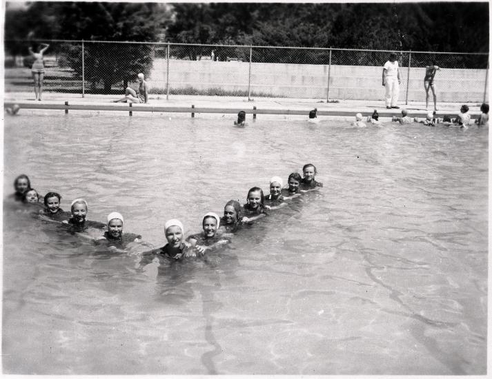 A group of female pilots in training during World War II swim together in a triangle formation in a pool.