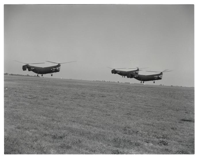 Three helicopters with two sets of propellors apiece vertically fly together during an airshow.