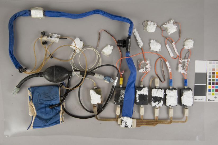 A during-conservation view of an blue Apollo program medical instrumentation harness. Majority of the harness and various parts have been removed from its previous white board.