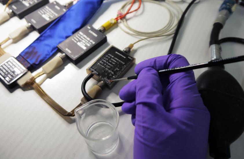 A Museum conservation specialist (seen wearing a purple glove) applies a coat of acrylic resin in the process of cleaning an Apollo program medical instrumentation harness.