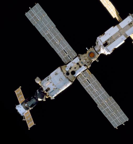 Bottom view of a section of the International Space Station with a cylinder-shaped module with one side attached to a smaller solar panel. The other side is attached to a much larger solar panel.