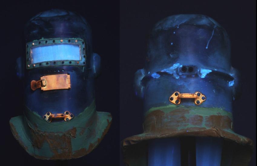 Side-by-side views of the Wiley Post pressure helmet, with the front visible on the left and the back visible on the right. Views are taken from ultraviolet light intended to discover corrosion products used on the helmet.