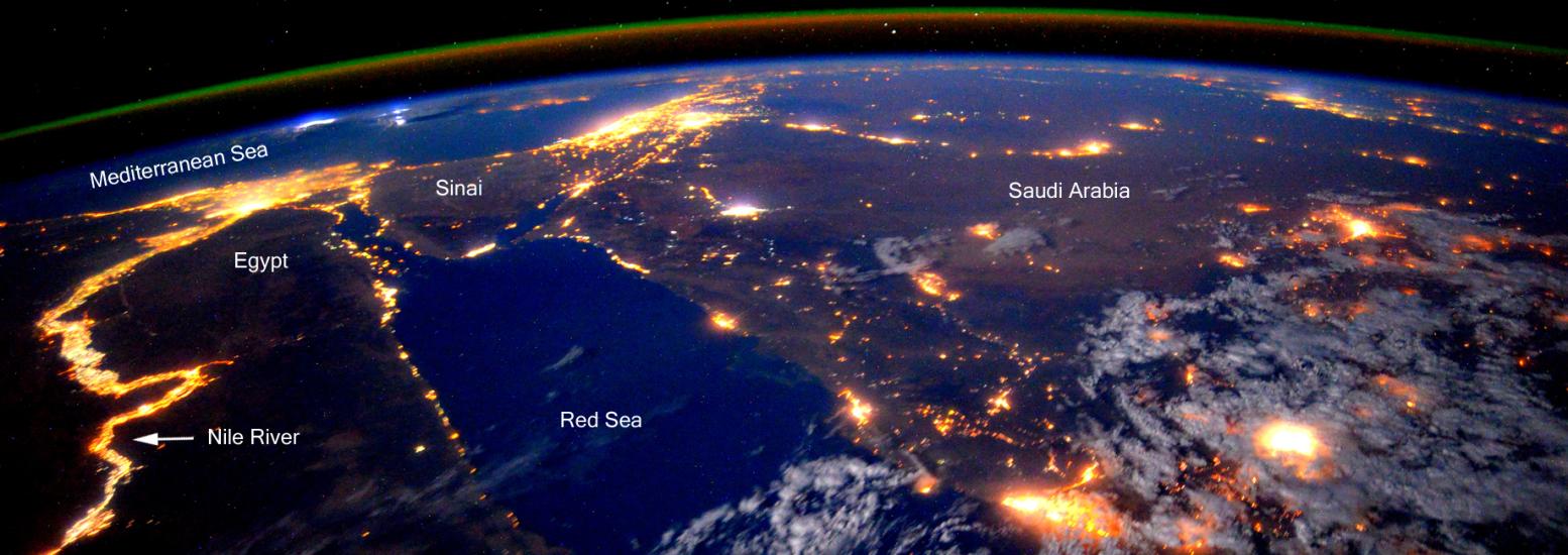 A partial satellite-style view of the Earth, with a focus on North Africa and the Middle East at night. Lights can be seen throughout heavily populated areas.