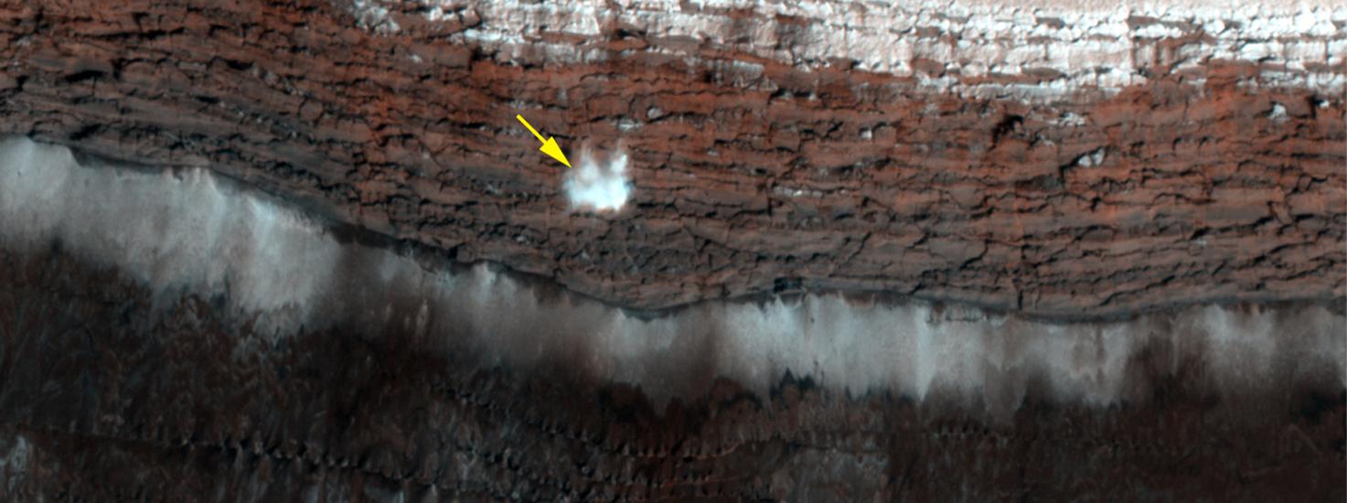 A frost-covered cliff on the northern polar surface of Mars. A yellow arrow points out potential frost that is in the process of freefalling.