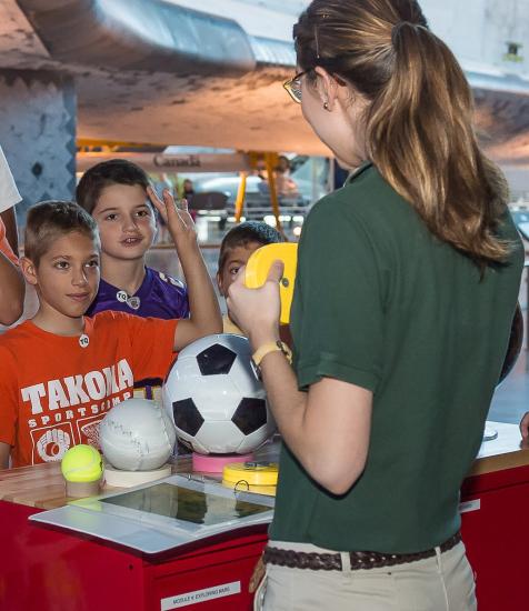 A Museum employee teaches multiple children about Mars as part of an astronaut game.