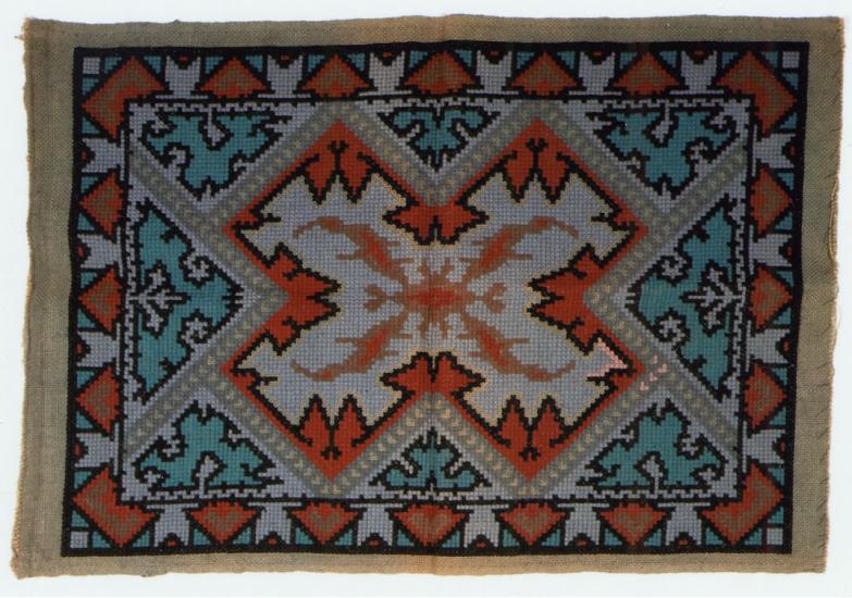 Orange, blue, and white knitted rug with intricate X-letter shape pattern.