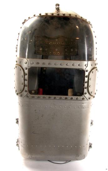 Small, metal capsule with two glass screens on the upper half. Two handles can be seen in the lower glass screen.