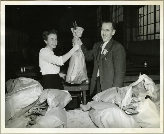 Two employees of an aeronautical corporation in the 1940s smile as one employee hands a turkey to the other employee.