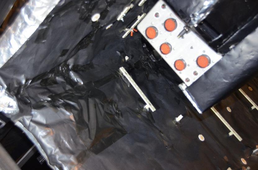 Sheets of black-colored material attached to double-sided tape are applied as part of restoring the Apollo Telescope Mount. Here, the black-covered material is placed as part of the cover of the spar.