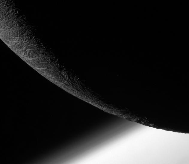 Partial view of the mostly non-illuminated Enceladus, a moon of Saturn.