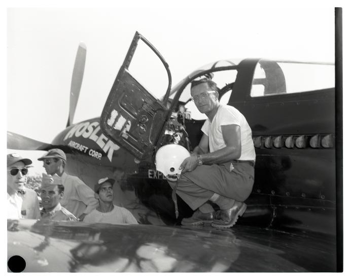 Robert Eucker, a white male aviator, stands on the wing of his aircraft. He is holding a white helmet.