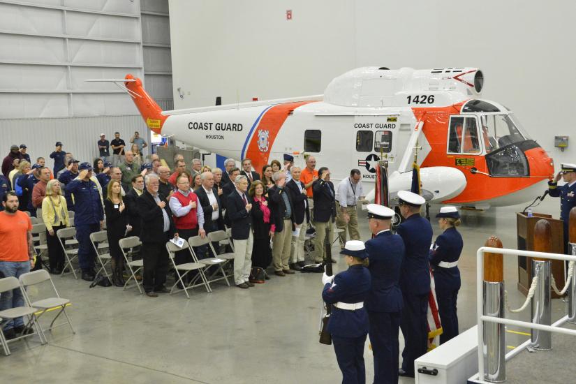 A group of people stand together for a ceremony following the restoration of an orange and white helicopter on their left .