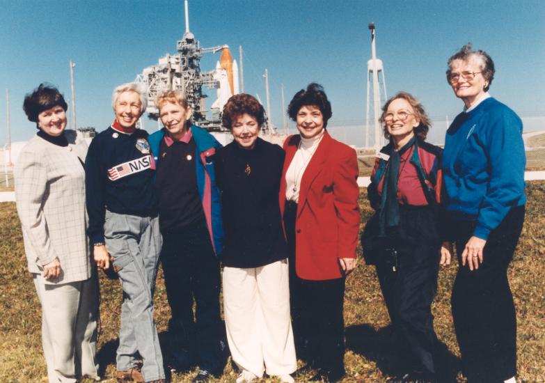 Seven women who trained to become astronauts in 1961 pose together in front of a Space Shuttle launch in 1995.