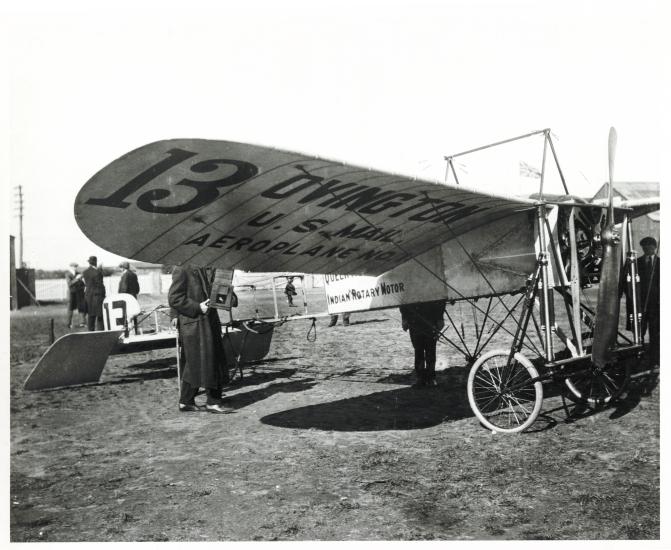 Side view of wooden and metal monoplane. Under the left wing, the plane is marked as owned by the "U.S. Mail".