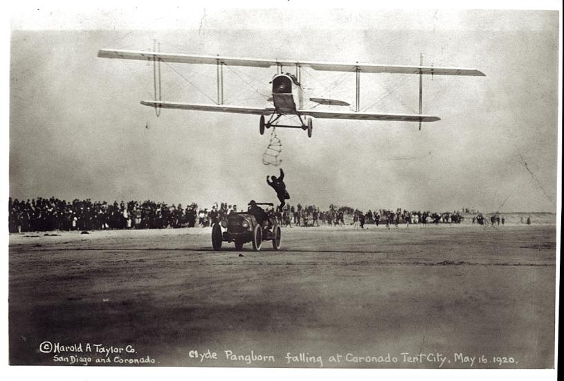 Front view of a biplane during an expedition flight. A person is trying to climb from an automobile below the biplane onto the biplane.