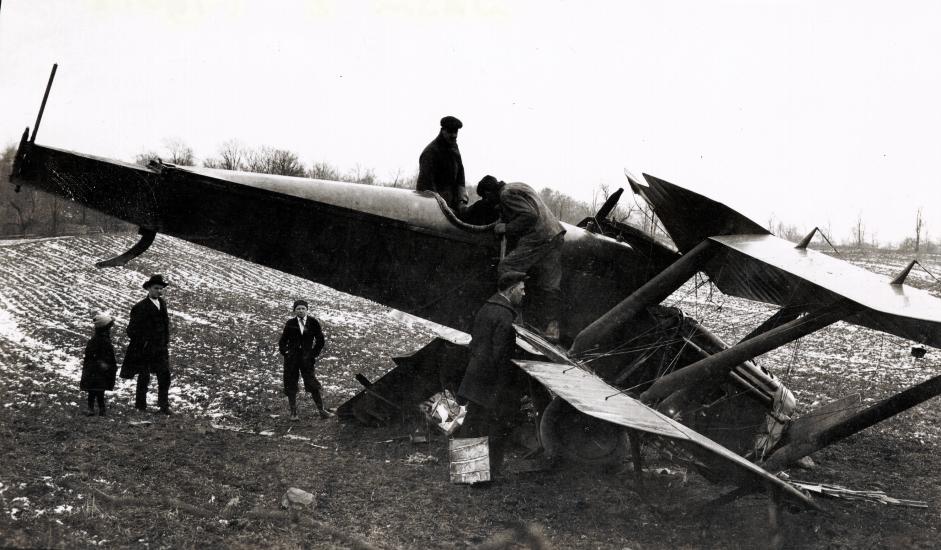 A crashed plane sits in a field and bystanders look at the plane.