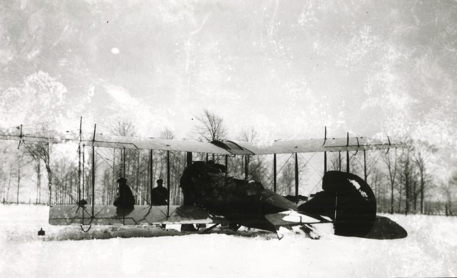 Front view of a biplane partially covered with materials as it stands on snowy ground in a snowstorm.