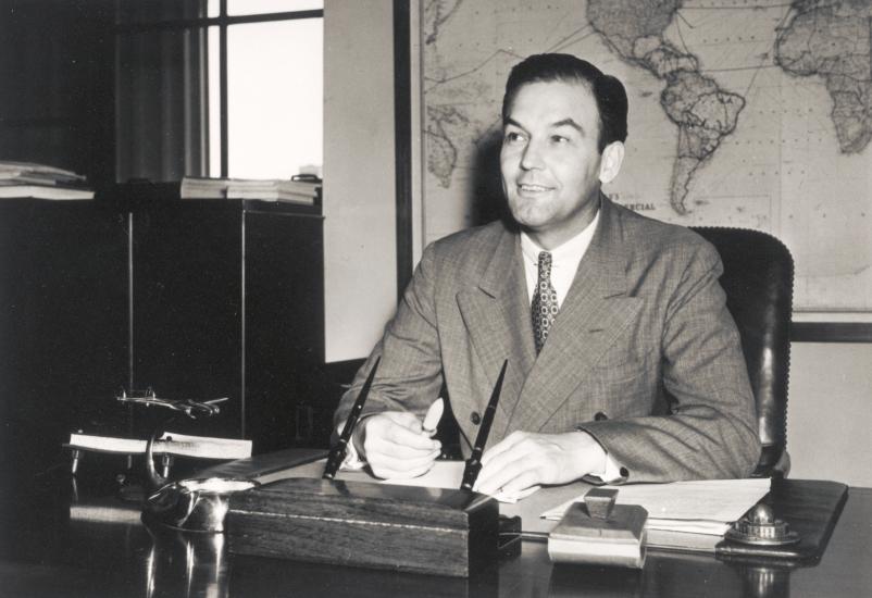 L. Welch Pogue, a white male chairman of the Civil Aeronautics Boards, poses informally as he sits at a desk.