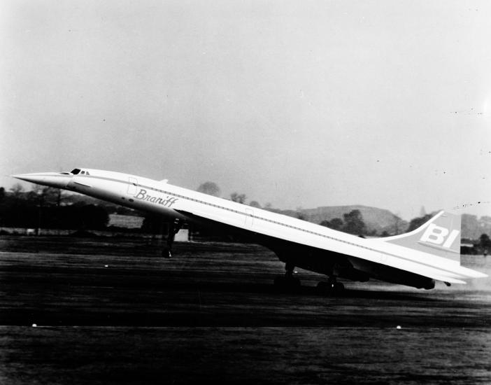 Artist's impression of the side view of a notably narrow aircraft with long back wings. The aircraft is taking off from an airport.