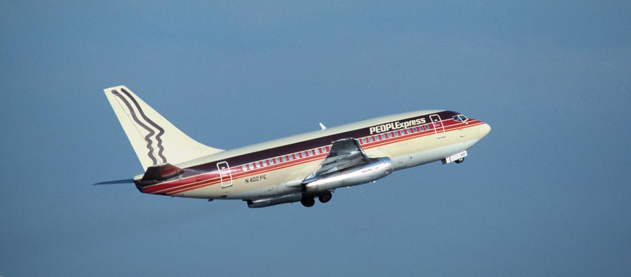 Side view of commercial aircraft in flight. Aircraft has at least two engines and red, black, and white PeoplExpress