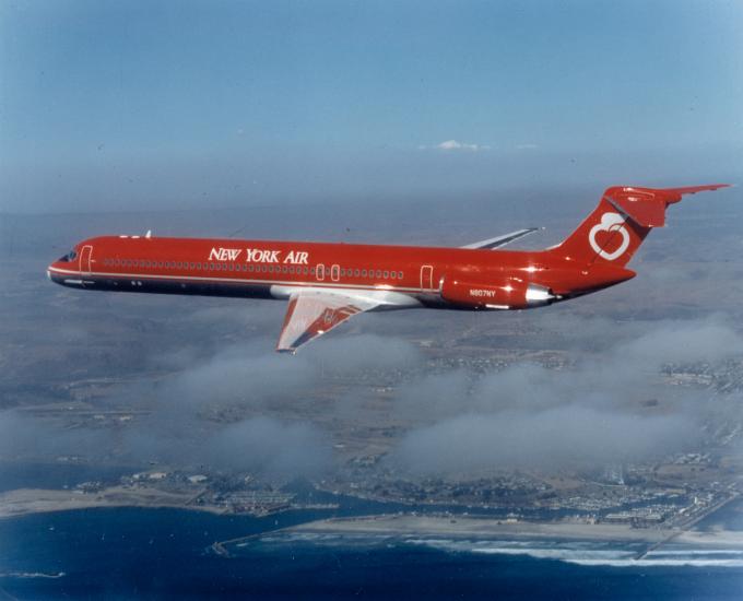 Side view of commercial jet in flight. Aircraft features red and white New York Air livery and two jet engines near the back of the plane.