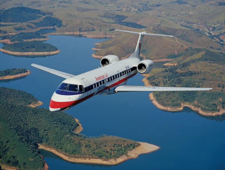 Front view of commercial jet in flight. The jet has two engines placed near the rear of the plane and white, blue, and red American Eagle livery.