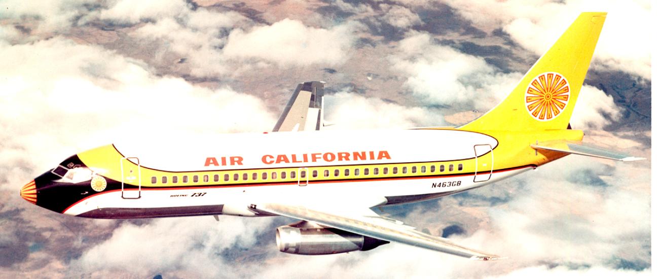 Side view of commercial aircraft in flight. Aircraft features two engines and white, yellow, black, and red Air California livery.