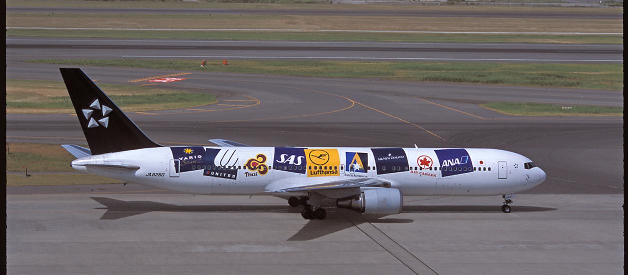 Side view of a commercial aircraft with multiple airline logos on the side of the aircraft.