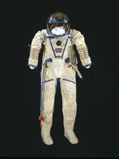 White pressure suit with blue trim and multiple plugs and tubes